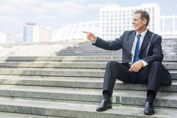 smiling-mature-businessman-pointing-something-while-sitting-staircase.jpg